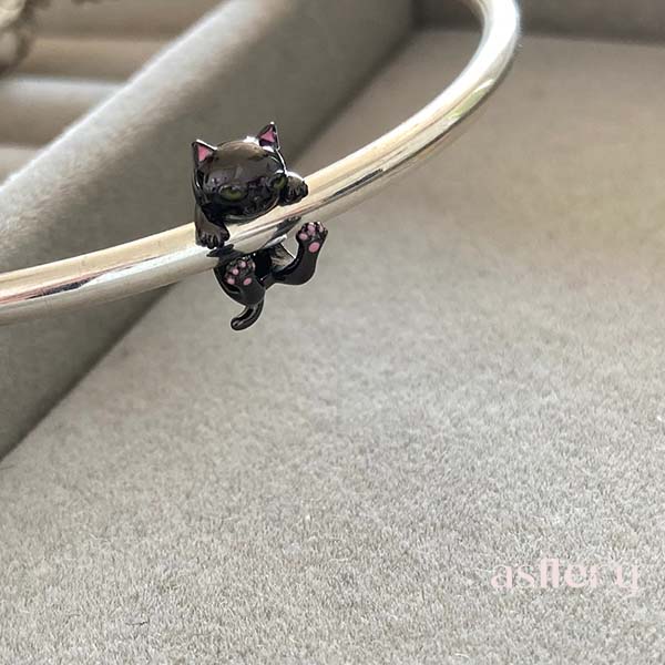 Stylized upside-down cat charm with black body, pink inner ears, and subtle floral-like paws, Asttery